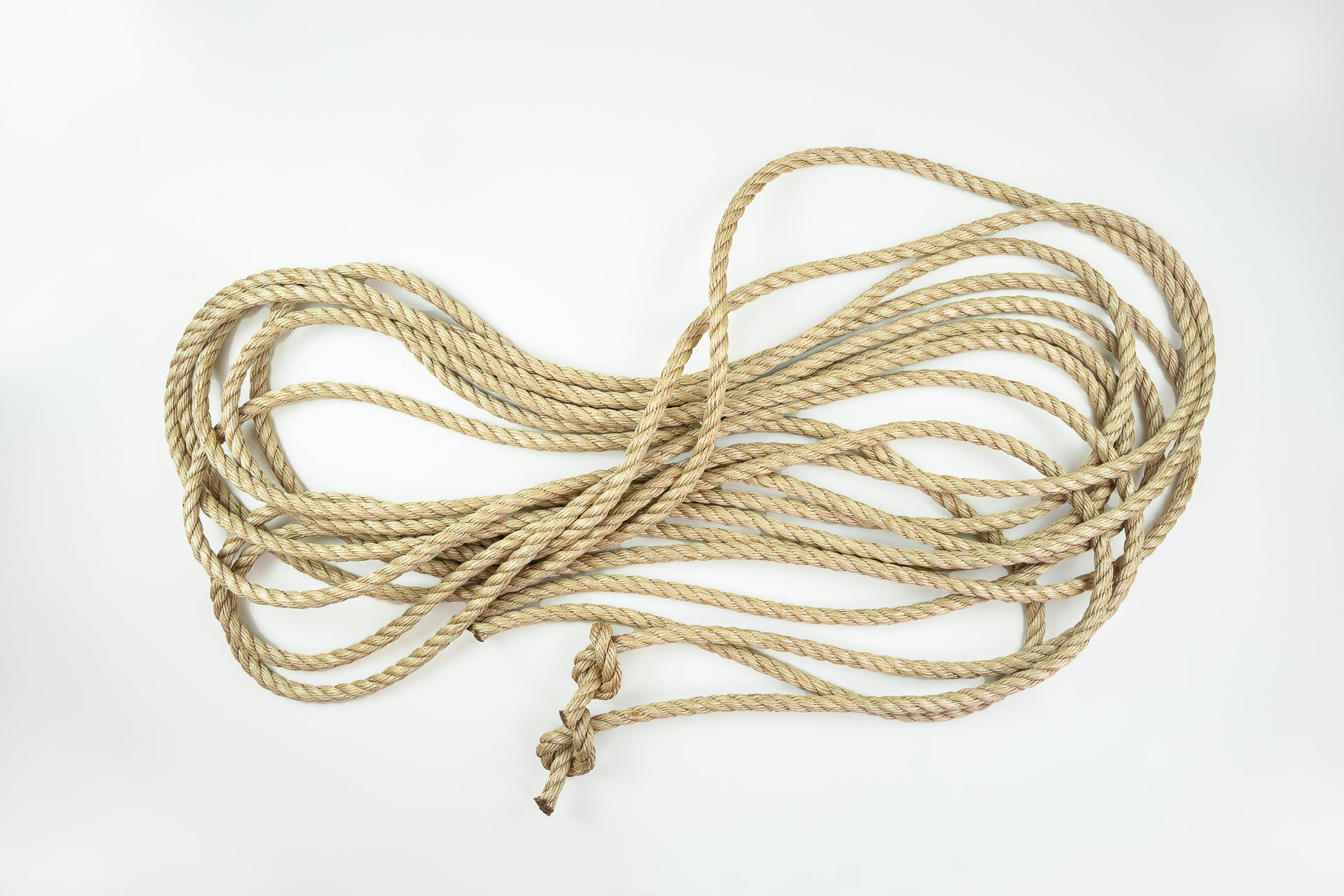 A beige-colored, twisted manila rope with a knot on one end, laid out in an entangled manner on a white background.