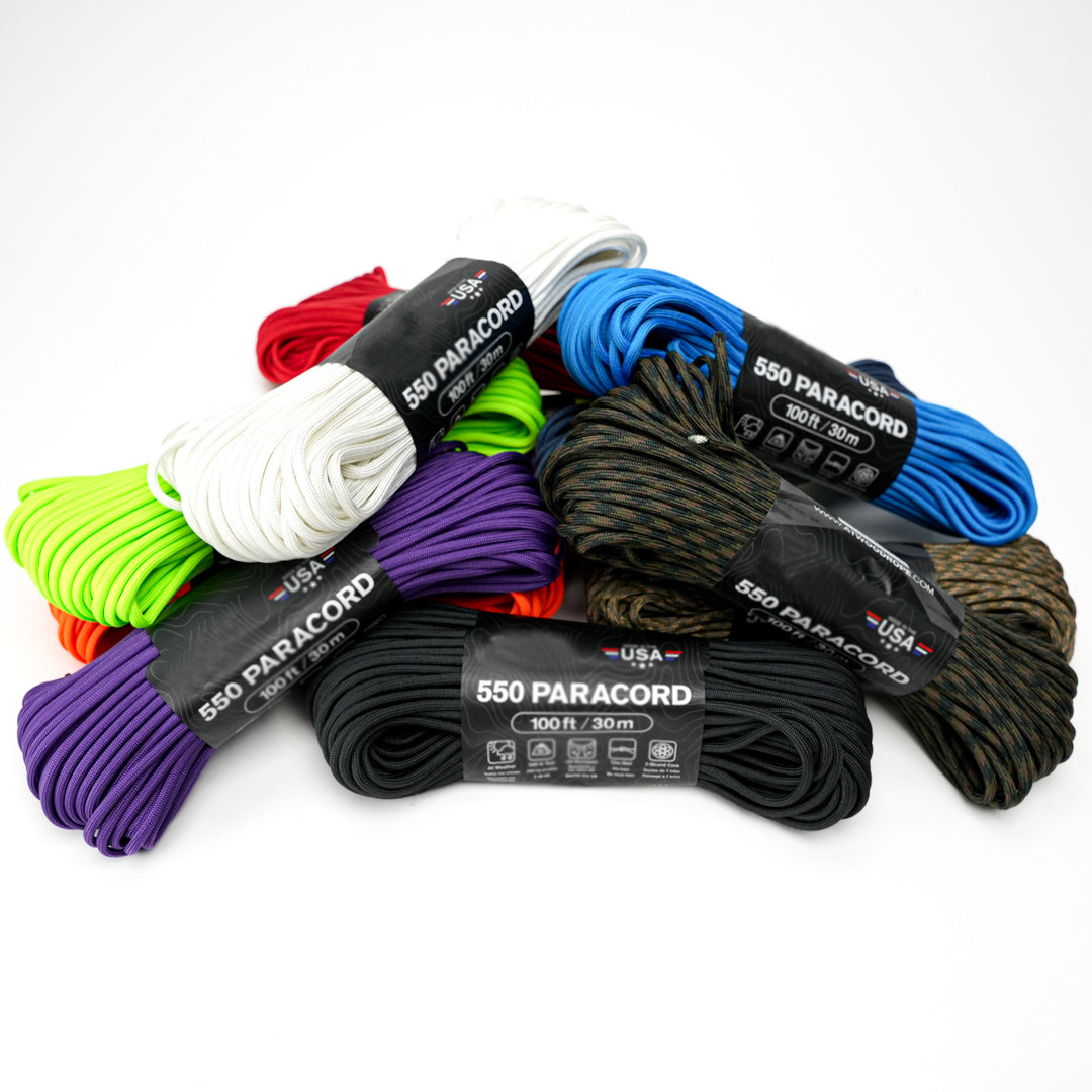 A collection of paracord ropes in various solid colors including black, blue, green, orange, purple, red, white, and yellow, coiled and labeled with '550 Paracord'.